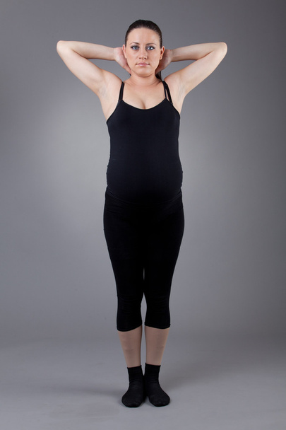 Pregnant woman doing gymnastic exercises on grey background. - Photo, image