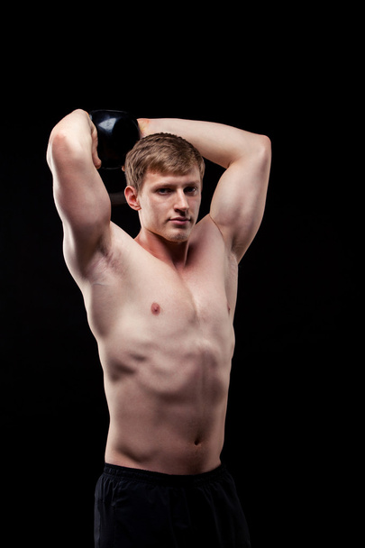 Handsome muscular guy with kettlebells isolated on black background - Foto, Imagem