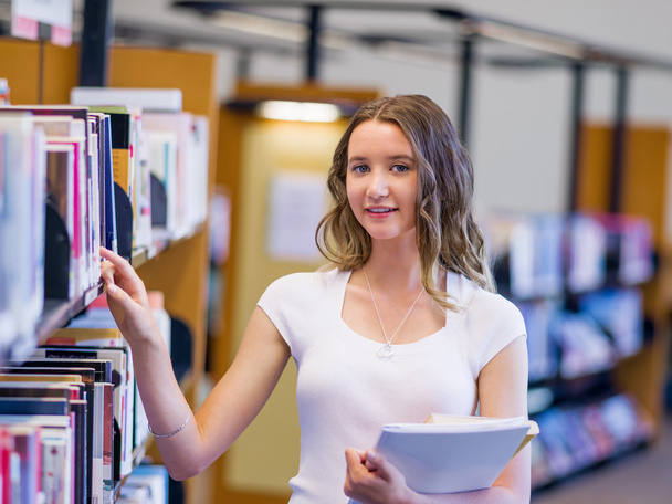 Happy female student holding books at the library - Фото, зображення
