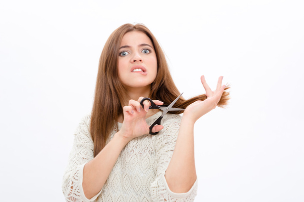 Unsure doubting pretty young woman cutting her hair - Φωτογραφία, εικόνα