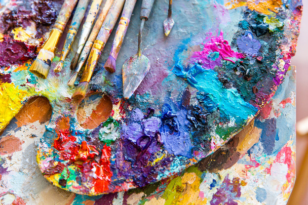 Closeup of art palette with colorful mixed paints and paintbrushed  - Zdjęcie, obraz