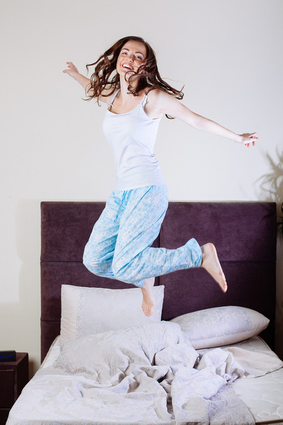 Happy young woman jumping on bed - Fotoğraf, Görsel