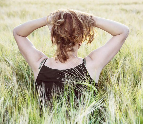 Jonge vrouw houdt haar haren door de zonsondergang in de weergave veld, achterste - Foto, afbeelding