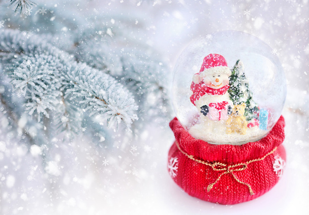 Um globo de neve com boneco de neve em um fundo coberto de neve ramos de abeto
 - Foto, Imagem
