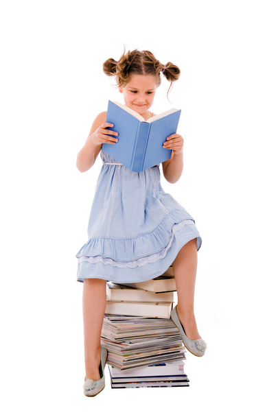 Image of schoolgirl sitting on the heap of books and reading one - Foto, Imagen