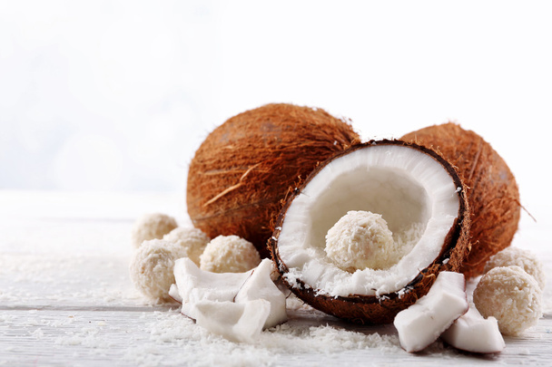 Candies in coconut flakes and fresh coconut on  light wooden background - Photo, image