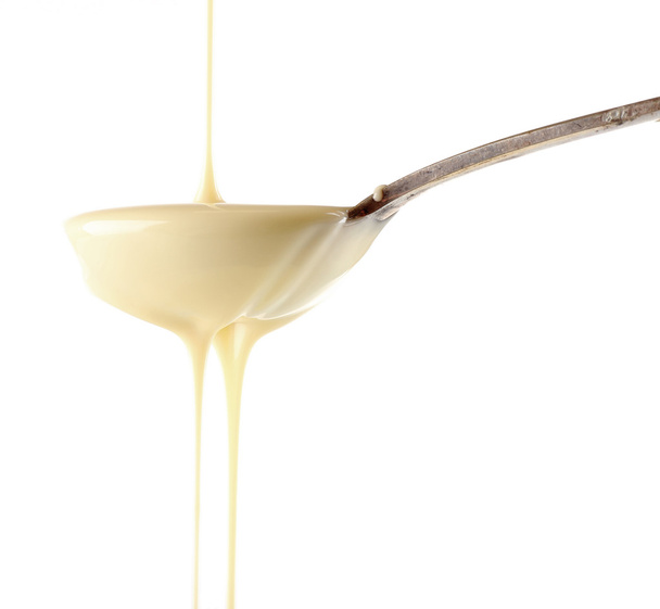 Condensed milk pouring from a spoon, isolated on white - Photo, image