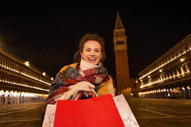 Smiling woman with shopping bags on Piazza San Marco in evening - Photo, image