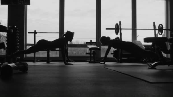 silhouette, two girls do push-ups together in a gym - Footage, Video