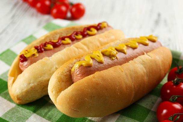 Delicious hot-dogs with tomatoes on green checkered cotton napkin, close up - Photo, image
