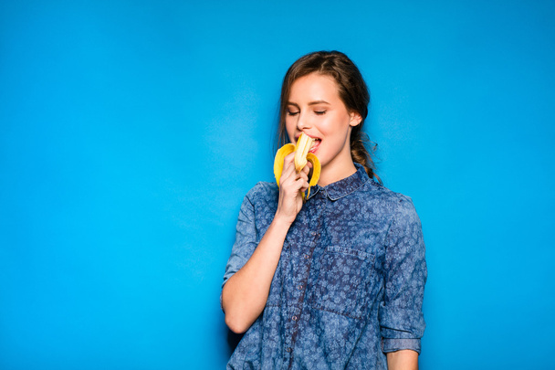 woman with banana in hands on blue background - Photo, image