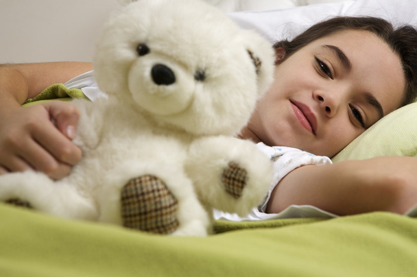 little girl lying in bed with bear  - Фото, изображение