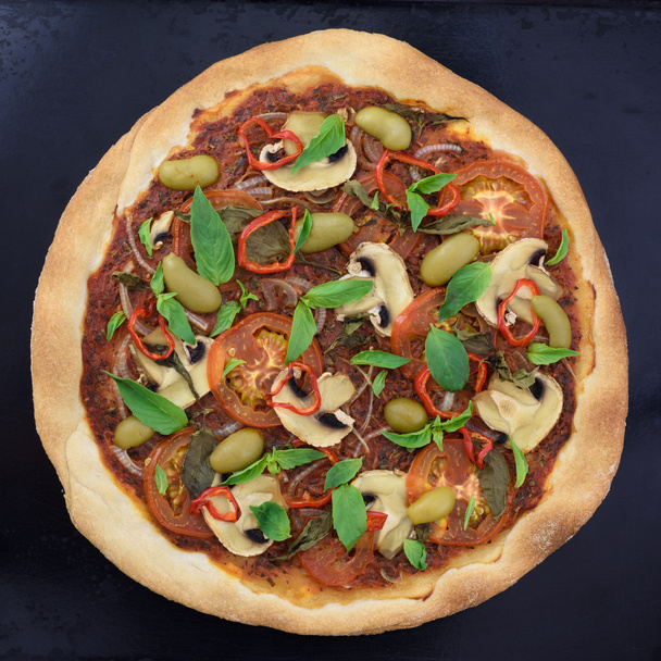 Appetizing pizza with mushrooms, basil and olives on black baking tray. Top view. - Photo, Image