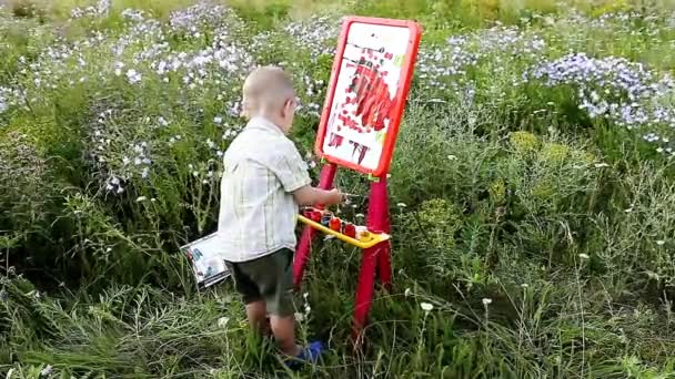 little boy paints on an easel outdoors - Footage, Video