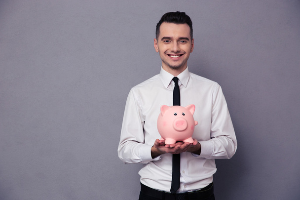 Smiling businessman holding pig money box - Foto, afbeelding
