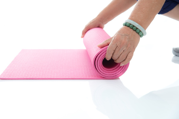 Senior hand's rolling pink yoga mat on white. - Foto, Bild