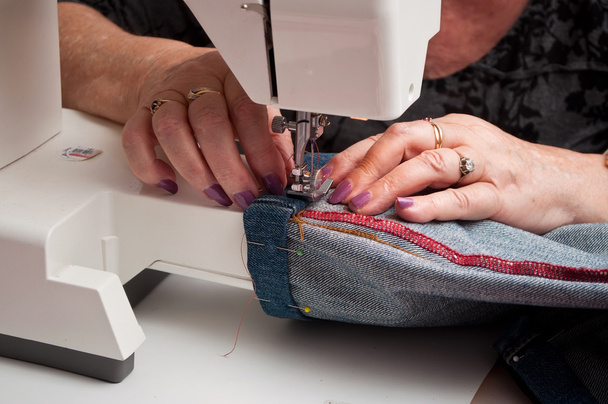 closeup of woman with a sewing machine and blue jeans hem - Foto, afbeelding