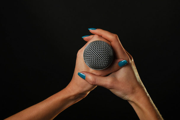 Frauenhände mit Mikrofon isoliert auf schwarz - Foto, Bild