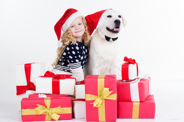 Child girl and white dog are sitting with gifts - Foto, afbeelding