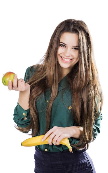 young beautiful girl in a green blouse holding an apple and a banana and smiling. isolate - Фото, зображення