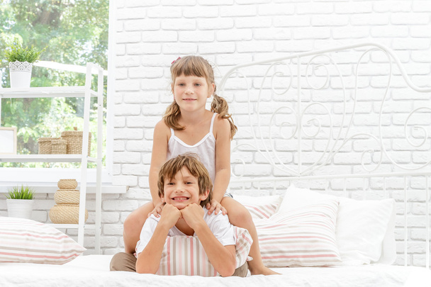 δύο παιδάκια ευτυχισμένος παίζει σε λευκό κρεβάτι στο σπίτι - Φωτογραφία, εικόνα