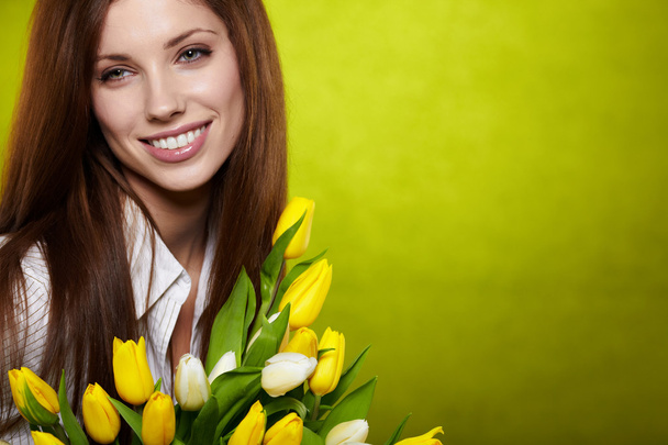 Smiling girl with yellow tulips. green background - Fotografie, Obrázek