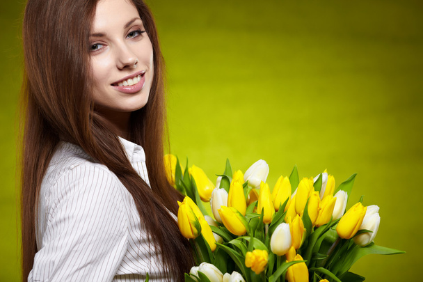 Smiling girl with yellow tulips. green background - Valokuva, kuva