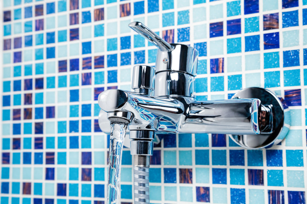Grifo de bañera en una pared de azulejos azules
  - Foto, imagen