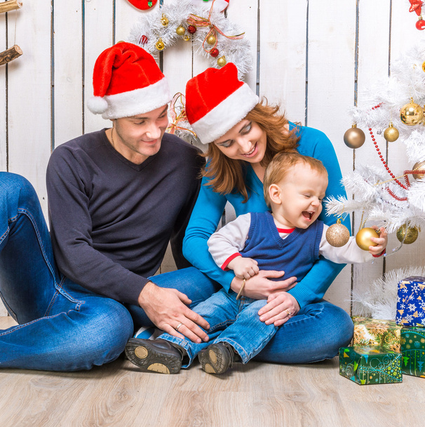 young family in red hats with little son near the christmas tree - Photo, image