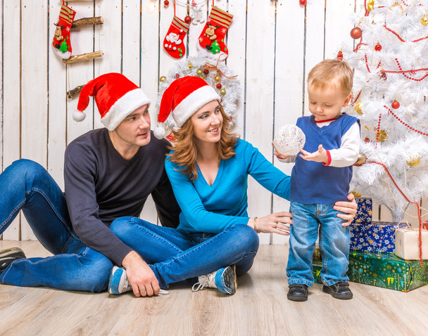 young family in red hats with little son near the christmas tree - Foto, Imagen