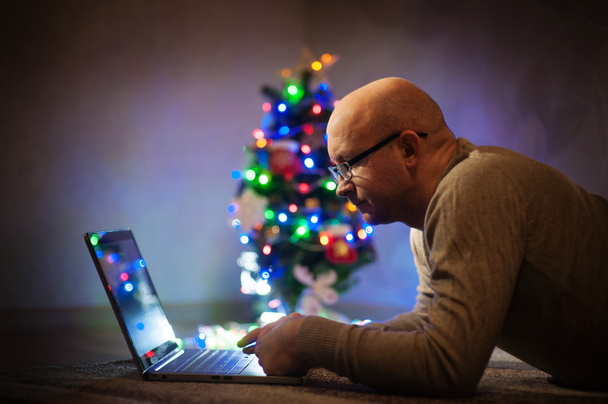 homem com óculos trabalhando em um laptop perto da árvore de Natal
 - Foto, Imagem