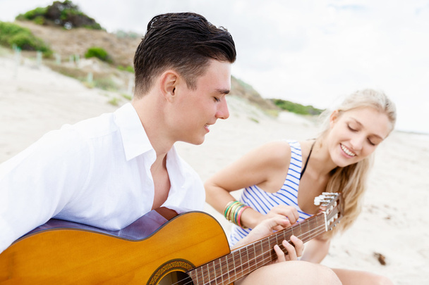 Νεαρό ζευγάρι παίζει κιθάρα στην παραλία στην αγάπη - Φωτογραφία, εικόνα