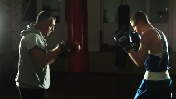 Silhouette of the trainer of the training young boxer on a ring - Footage, Video
