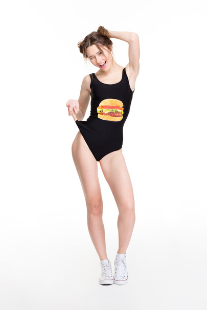 fröhlich zwinkernde junge Frau in schwarzer Badebekleidung mit Hamburger-Print  - Foto, Bild
