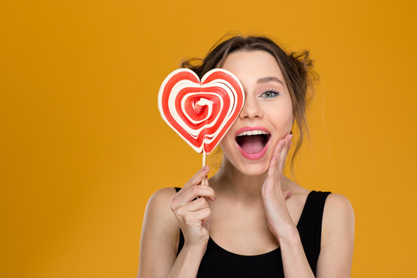 Happy excited woman covered her eye with heart shaped lollipop  - Fotografie, Obrázek