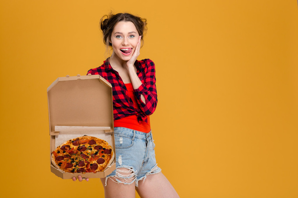 Amusing attractive young woman showing tongue and holding pizza - Фото, зображення