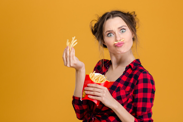 Funny pretty young woman making fake moustache with fries - 写真・画像