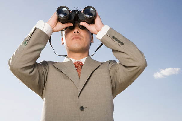Businessman looking through binoculars in desert - Photo, Image