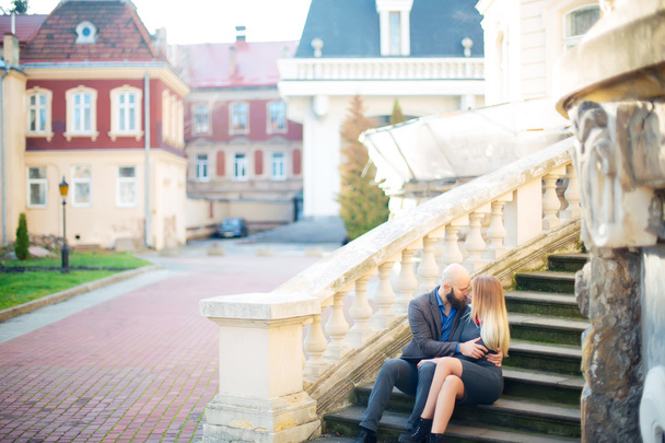 One beautiful stylish couple of young woman and senior man with long black beard sitting embracing close to each other outdoor in autumn street on stairs sunny day, horizontal picture - Φωτογραφία, εικόνα