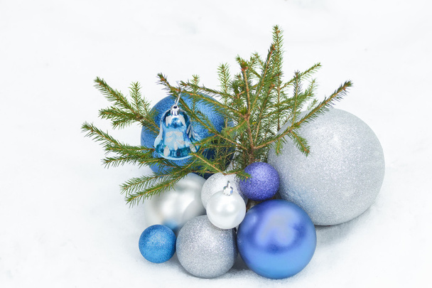 Árvore de abeto jovem no chão nevado com prata de Natal e ornamentos azuis na parte inferior
 - Foto, Imagem