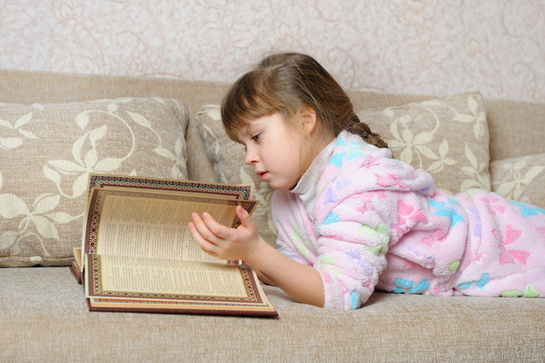 The little girl reads the book lying on a sofa - Valokuva, kuva