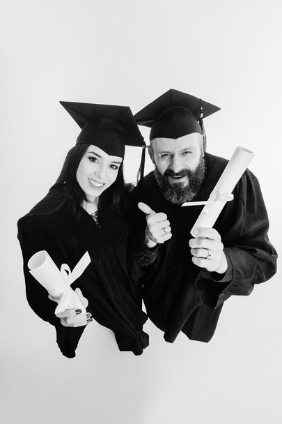 Δύο ευτυχισμένη ενηλίκων φοιτητές που αποφοιτούν απομονώνονται σε γκρι φόντο μαύρο και άσπρο - Φωτογραφία, εικόνα