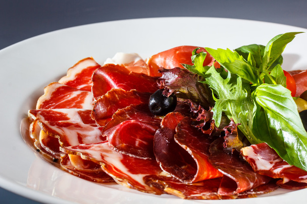 Sliced prosciutto, bacon and other meats are on the Board. - Fotó, kép