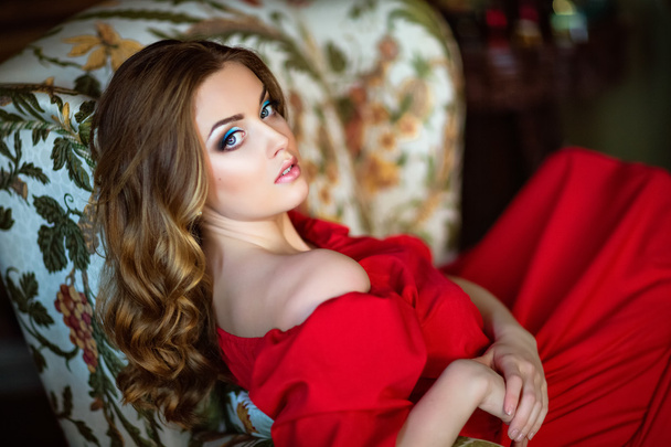 Portrait of a very beautiful sensual girl in red dress sitting on chair - Zdjęcie, obraz