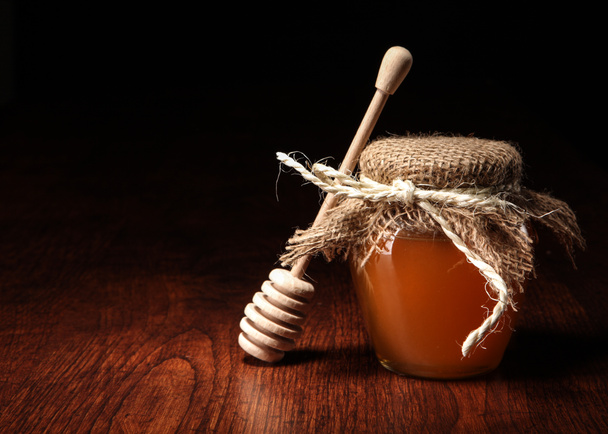 Pot of honey and wooden stick are on a table. - Photo, Image