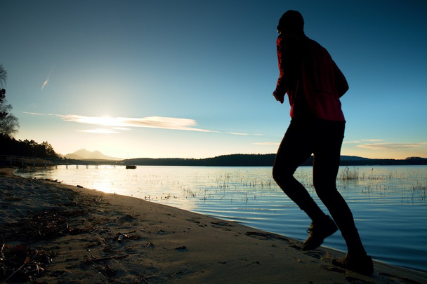 Sportovní muž dělá ranní běhání na mořské pláži na Bright Sunrise siluety - Fotografie, Obrázek