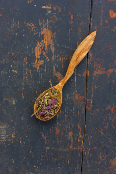 Dried herbs (Salvia officinalis) in a wooden spoon on the old cracked black background. Ingredient for cooking healthful beverage. The concept of rustic herbal therapy. Ingredient for cooking healthful beverage - Photo, Image
