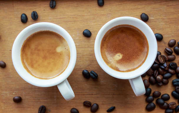 Dos cafés expresos en pequeñas tazas blancas, con un descanso de grano de café
 - Foto, imagen