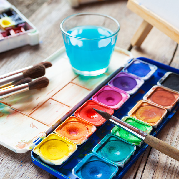 Watercolor paints, brushes and glass of water on old table - Fotografie, Obrázek