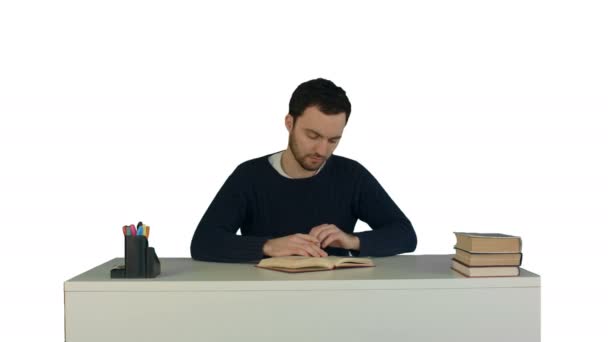 A young man reading a book on laptop on white background isolated - Záběry, video